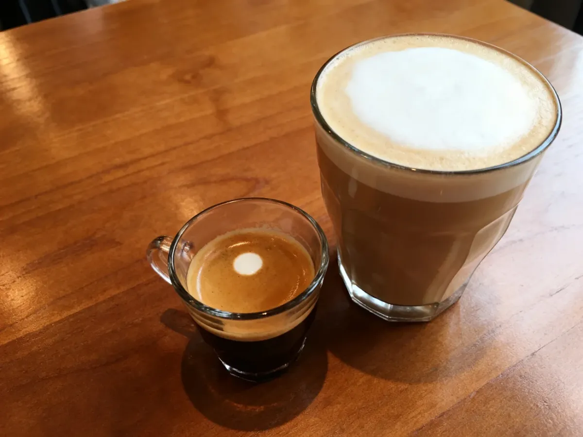 Espresso macchiato w małej filiżance obok większego cappuccino z puszystą pianką